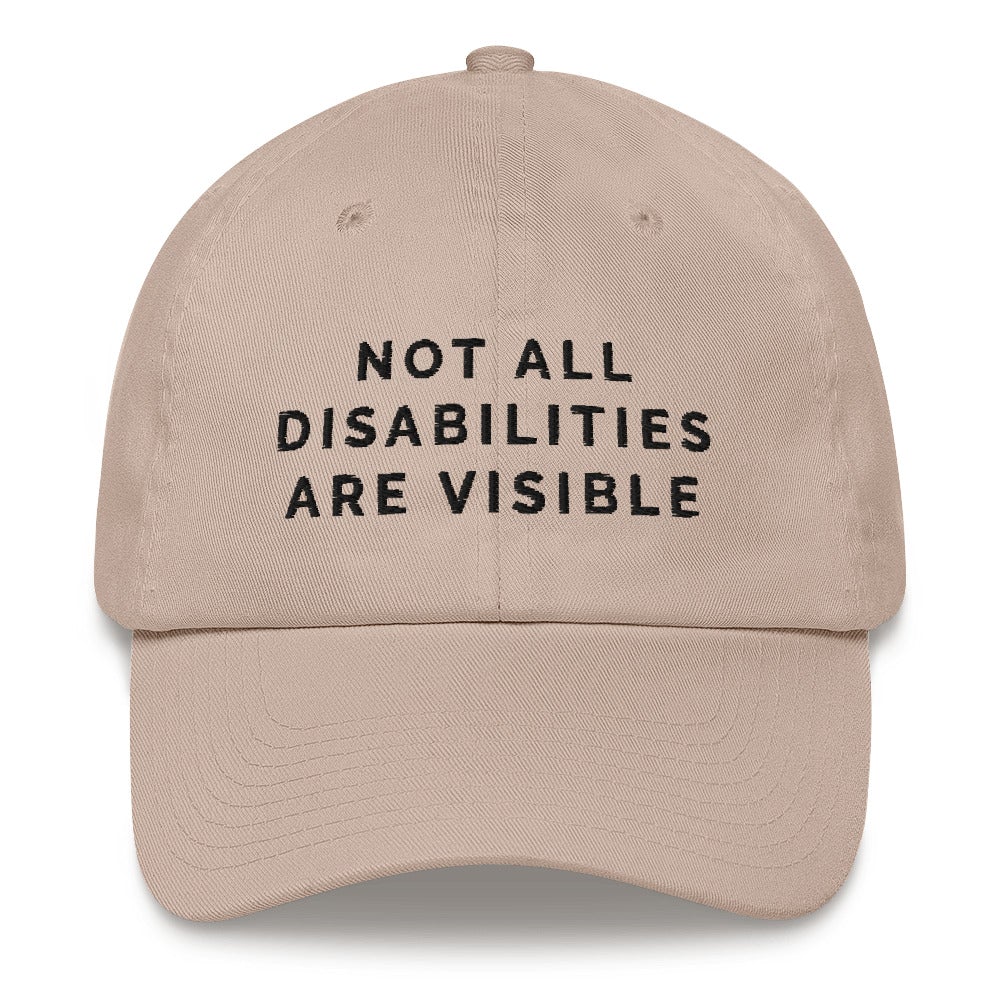 This is a photo of the front of a stone-colored Not All Disabilities Are Visible Cap. In the middle of the cap, in black embroidered upper case letters, is the phrase "Not All Disabilities Are Visible." The phrase is on three lines: (1) not all, (2) disabilities, (3) are visible.