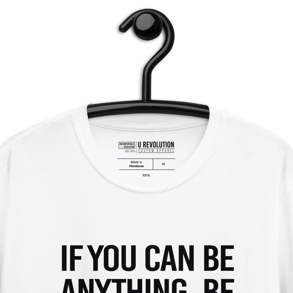 This is a photo of a white Be Inclusive White Basic Tee. On the front of the t-shirt, the phrase, 'If you can be anything, be inclusive,' is printed in black capital letters. The tee is on a black hanger and the inside URevolution t-shirt label is visible.