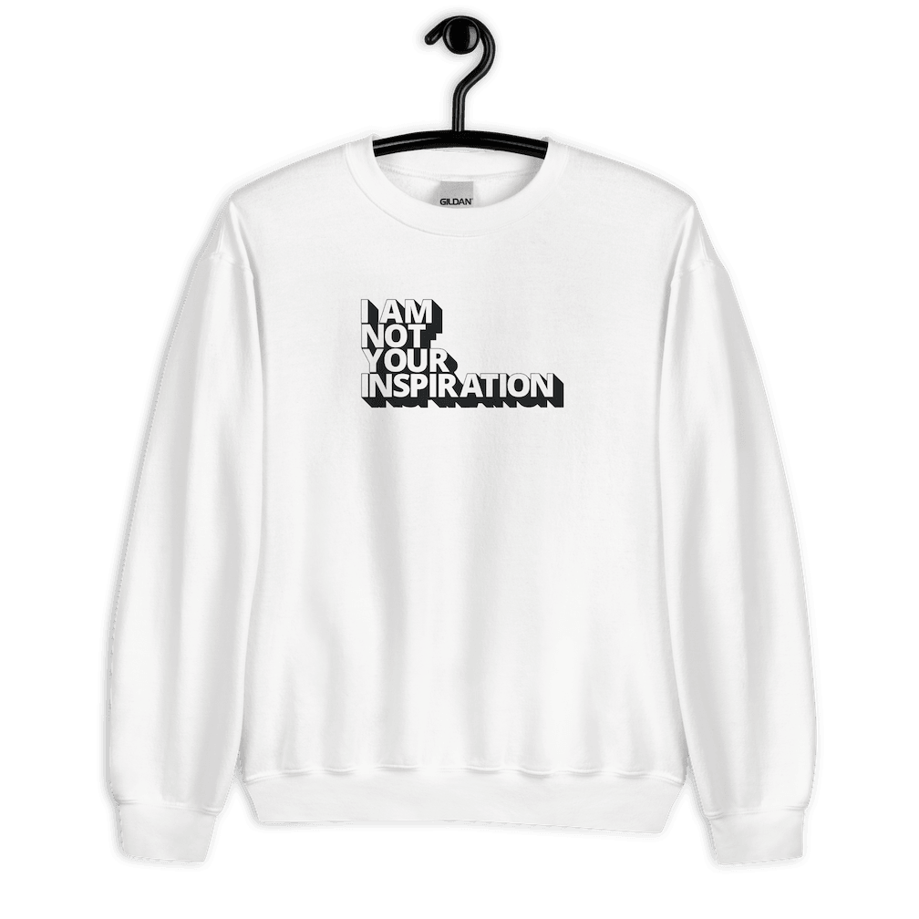 A white Not Your Inspiration sweatshirt. On the top third of the inspiration shirt is the phrase, "I am not your inspiration," printed over four lines in white upper case letters with a black retro shadow. The sweatshirt is hanging on a black hanger.