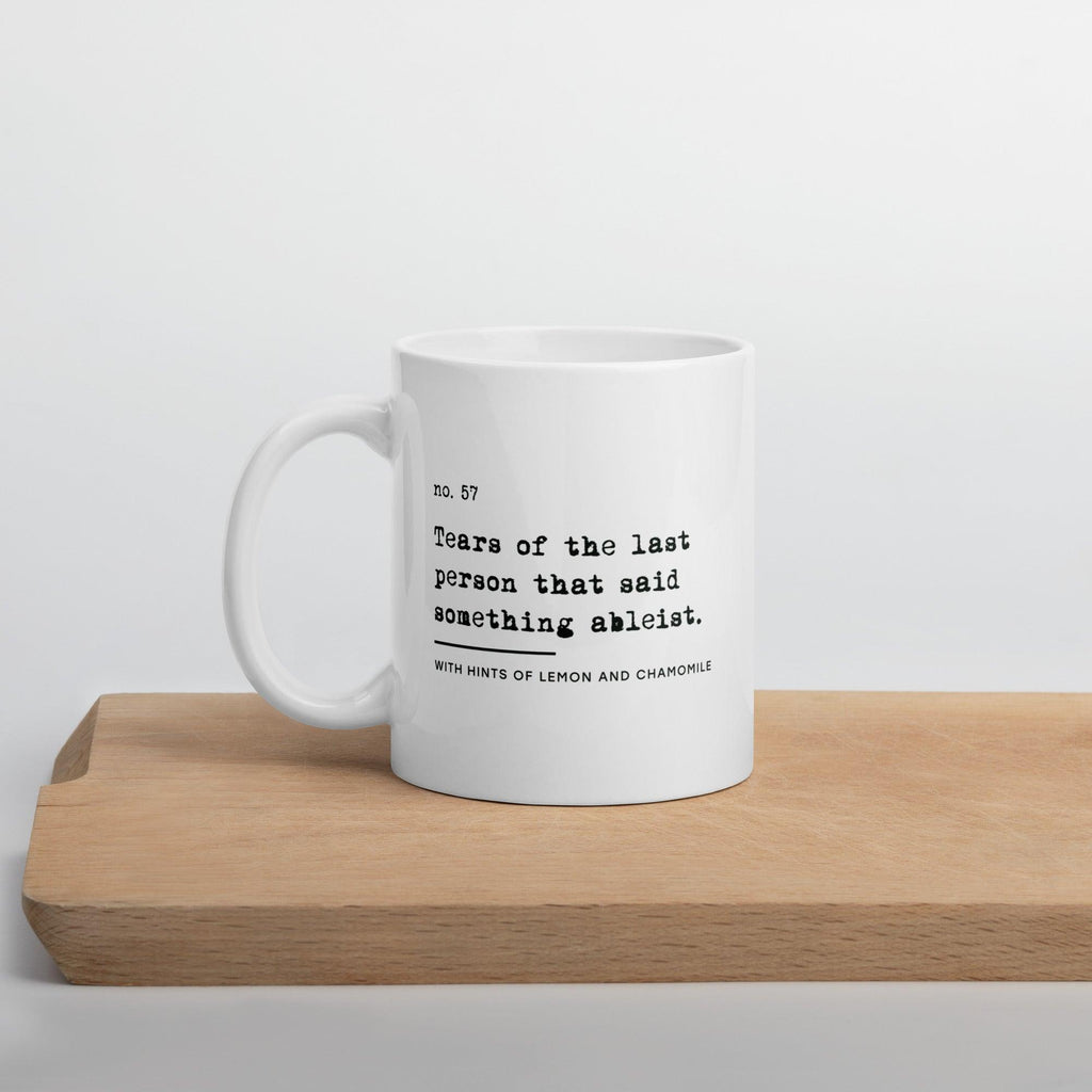 The ableist tears mug is white, with black text that reads: "no. 57. Tears of the last person that said something ableist. With hints of lemon and chamomile." 