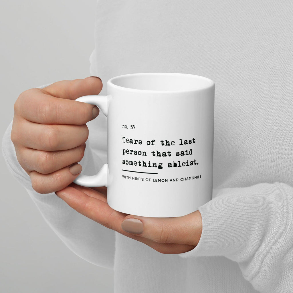 The ableist tears mug is white, with black text that reads: "no. 57. Tears of the last person that said something ableist. With hints of lemon and chamomile." 