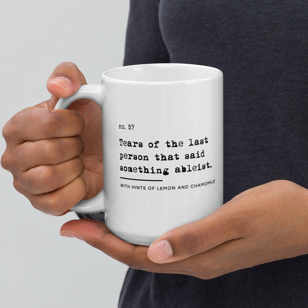 The ableist tears mug is white, with black text that reads: "no. 57. Tears of the last person that said something ableist. With hints of lemon and chamomile." 
