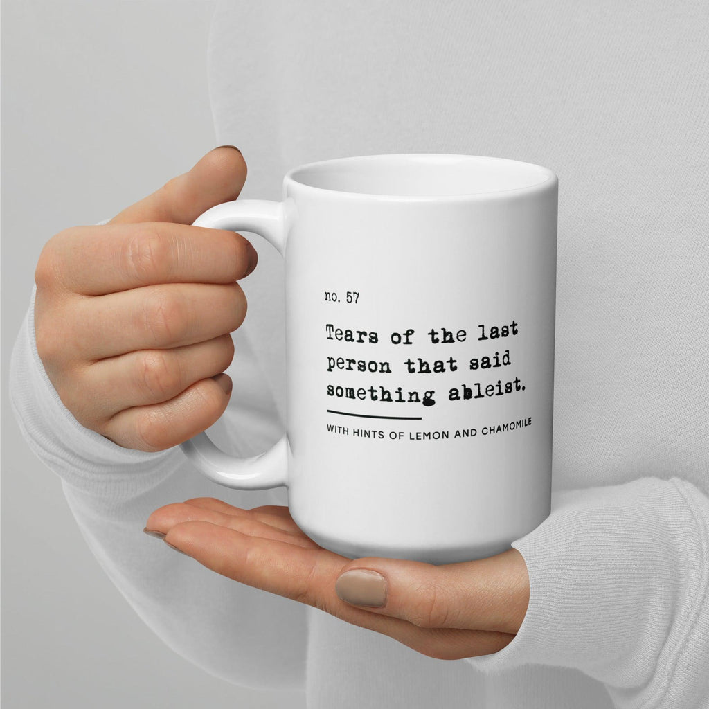 The ableist tears mug is white, with black text that reads: "no. 57. Tears of the last person that said something ableist. With hints of lemon and chamomile." 