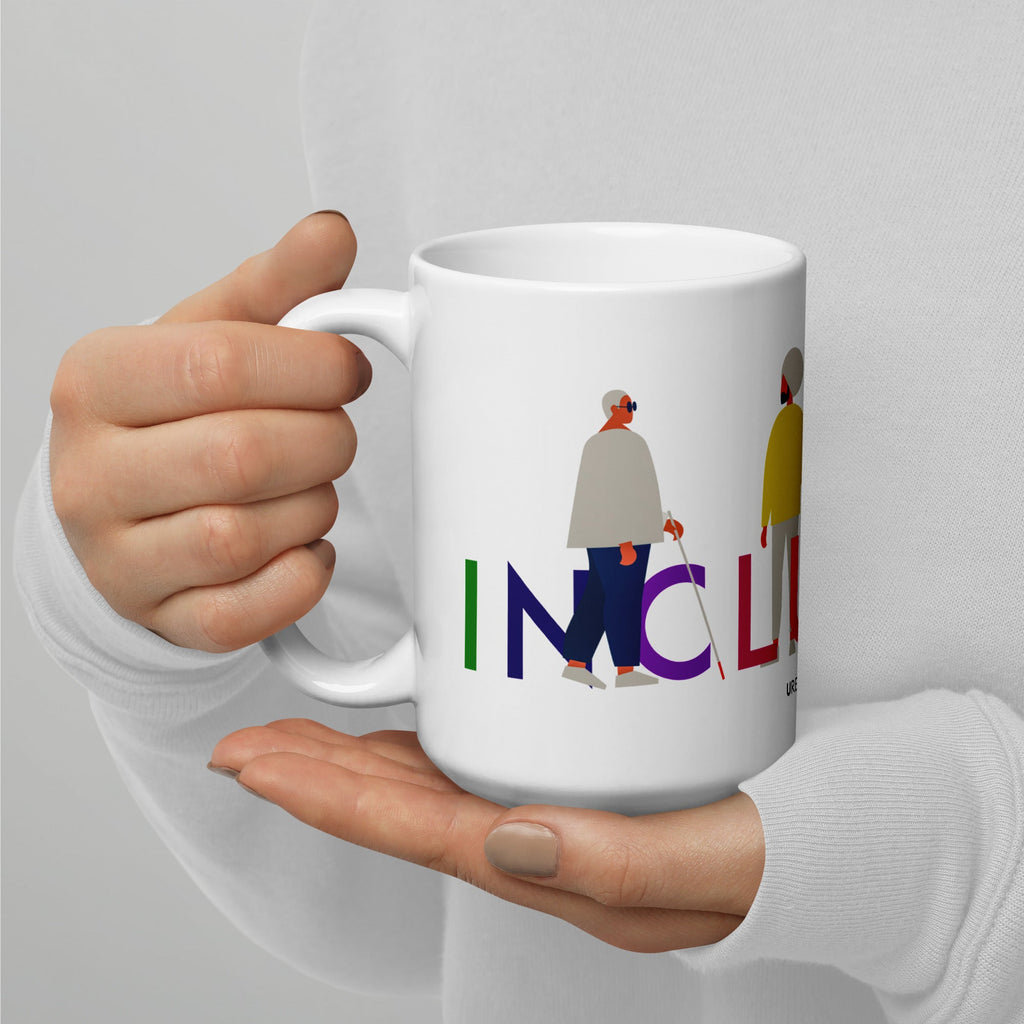 This is a photo of a white inclusion mug with URevolution's Inclusion icon on the side. The word INCLUSION is written in all caps in rainbow colors. Among the letters are four characters: one plus-sized person with glasses and a cane, one person with one arm wearing a turban, one person with long hair and a prosthetic leg, and one person with an afro, seated in a wheelchair.