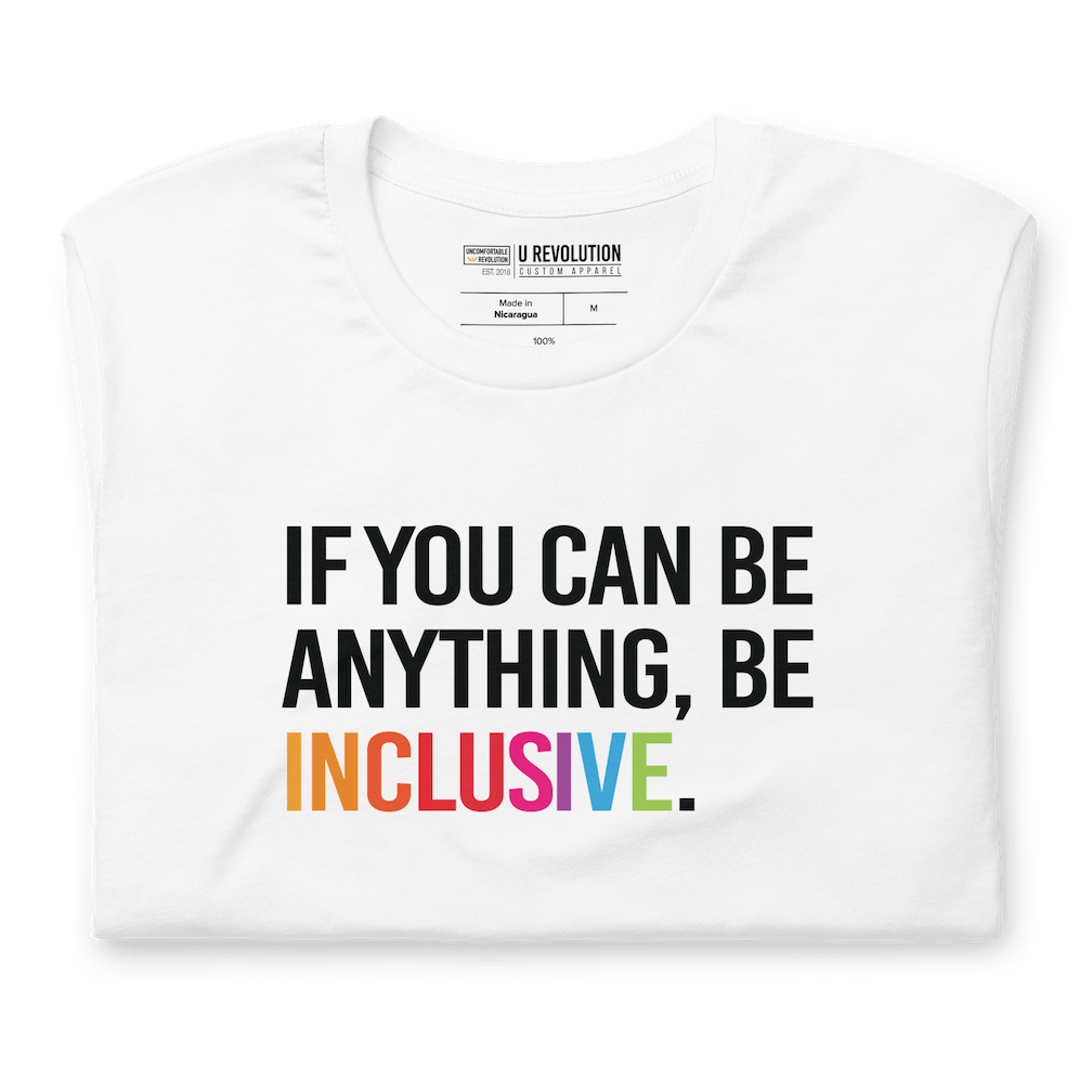 This is a photo of a white rainbow classic Be Inclusive tee. On the front of the inclusive t-shirt is the phrase: "If you can be anything, be inclusive," in black upper case letters. All the text is in black, except "Inclusive," which is in rainbow colors.