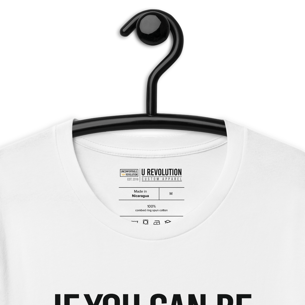 This is a photo of a white rainbow classic Be Inclusive tee. On the front of the inclusive t-shirt is the phrase: "If you can be anything, be inclusive," in black upper case letters. All the text is in black, except "Inclusive," which is in rainbow colors.