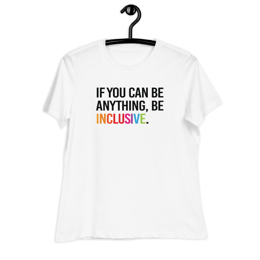 This is a photo of a white relaxed-cut Be Inclusive Tee Be against a plain background. On the front of the t-shirt, the phrase, 'If you can be anything, be inclusive,' is printed in black capital letters.   The word "Inclusive" is in rainbow colors. The tee is hanging on black hanger.